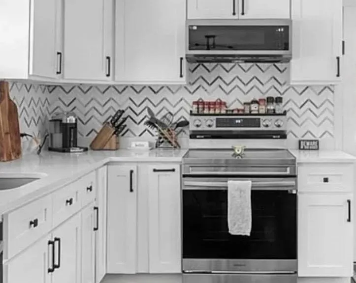 Updated kitchen with ample white cabinetry, generous counters, and stainless steel range with vent hood and tile backsplash.