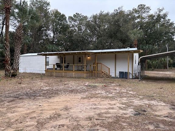 Back Porch view with covered walkway to carport provides a rain free access to the house. This peaceful retreat is large enough for a large outdoor dining table OR couch/chair set. Wonderful wildlife views.