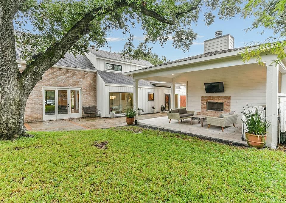 Covered outdoor patio and kitchen features stone flooring, gas/wood fireplace with brick hearth, stone countertop and gas grill.