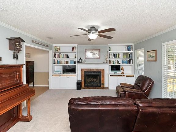 Living area featuring a tiled fireplace, ceiling fan, carpet flooring, and a textured ceiling