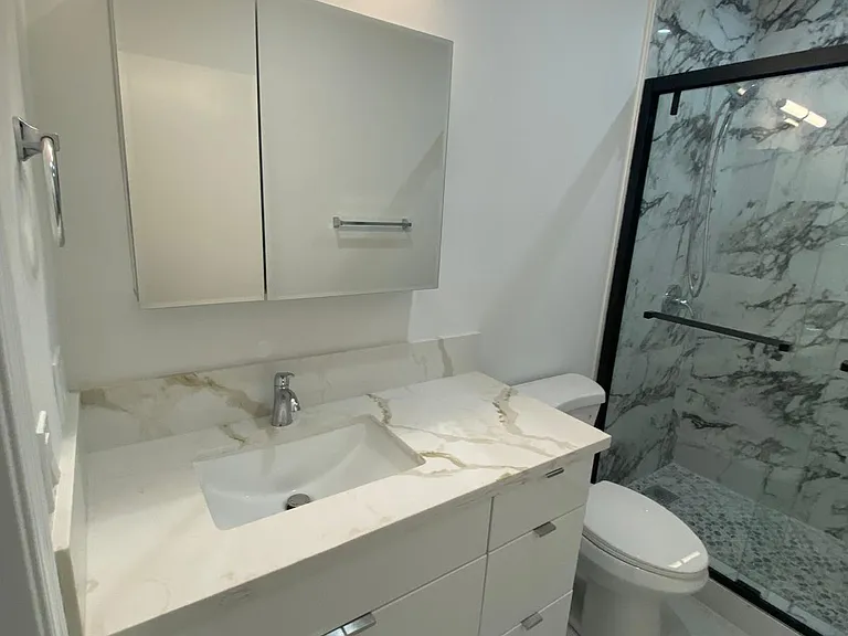 Modern bathroom featuring a white vanity, modern mirror lighting, toilet, and glass-enclosed marble-look shower.