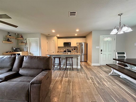 Open-concept living area featuring wood-finish flooring, a kitchen island with bar seating, stainless steel appliances, and recessed lighting