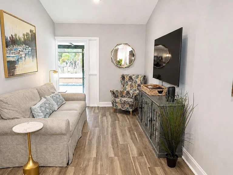 Living room with a sofa, accent chair, media console and wall-mounted TV, plus a door to the outdoor area.