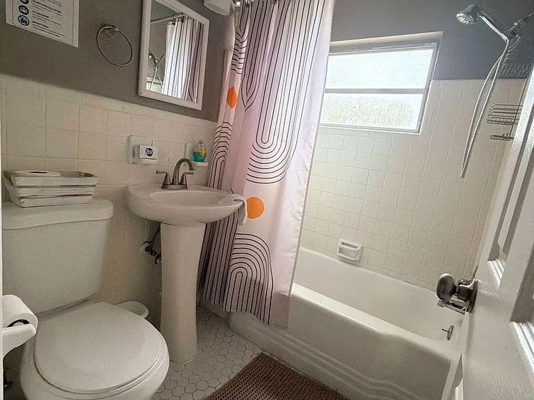 Full bathroom with a tub/shower combo, tiled surround, and pedestal sink, plus a frosted window for natural light.