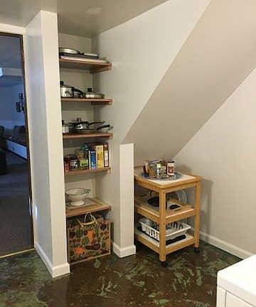 Kitchenette with stove, sink and garbage disposal, refrigerator, cabinets and open shelving for storage. Washer and Dryer face the open shelves.