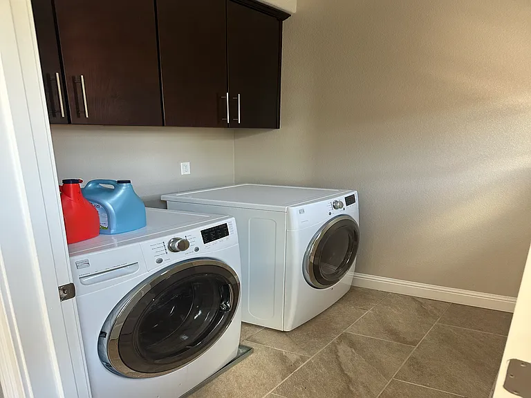 Convenient in-unit laundry room featuring high-efficiency washer and dryer plus upper cabinetry for storage.