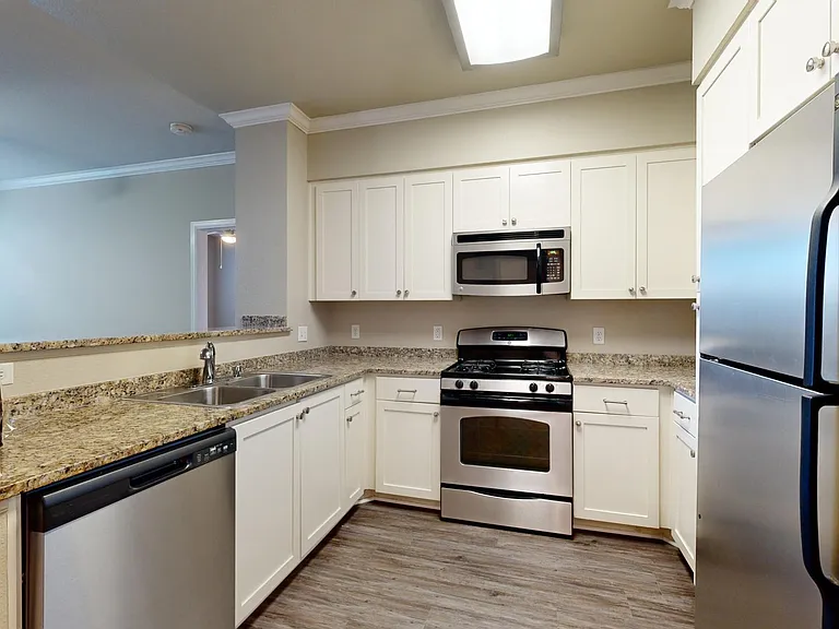 Apartment kitchen with stainless steel appliances, granite countertops, and wood-style flooring.