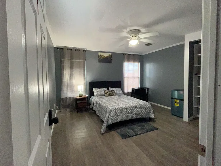 Private bedroom with wood-look floors, ceiling fan, and space for a full bed plus desk; two windows add natural light.