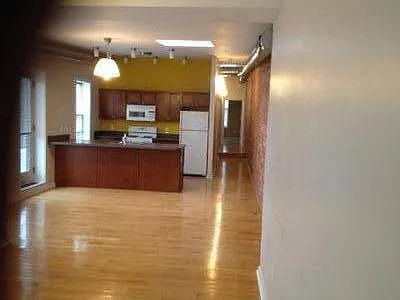 Empty view of living area looking toward the kitchen and hallway to the bathroom and second room on the right and the larger bedroom at the end.