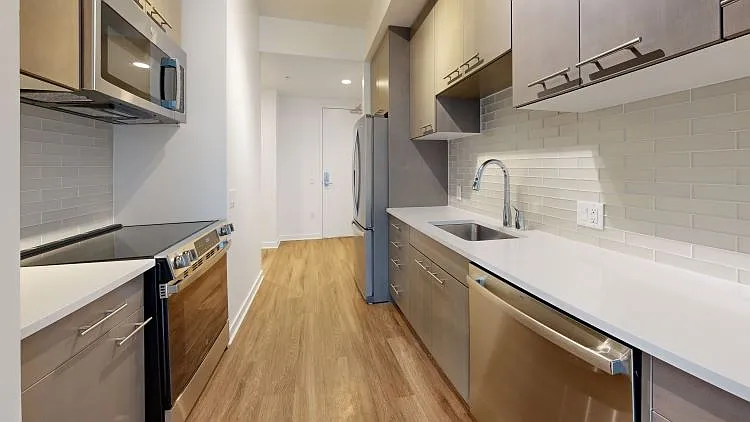 Apartment kitchen with stainless steel appliances, quartz countertops and wood-style flooring.