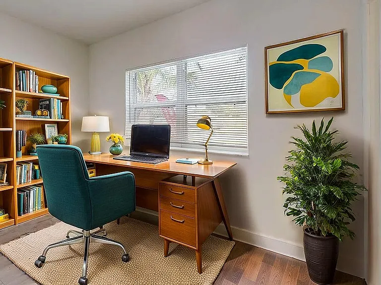 Charming home office with vibrant decor, featuring a stylish desk, teal office chair, large bookshelf with colorful books, and a lush indoor plant for a refreshing work environment.