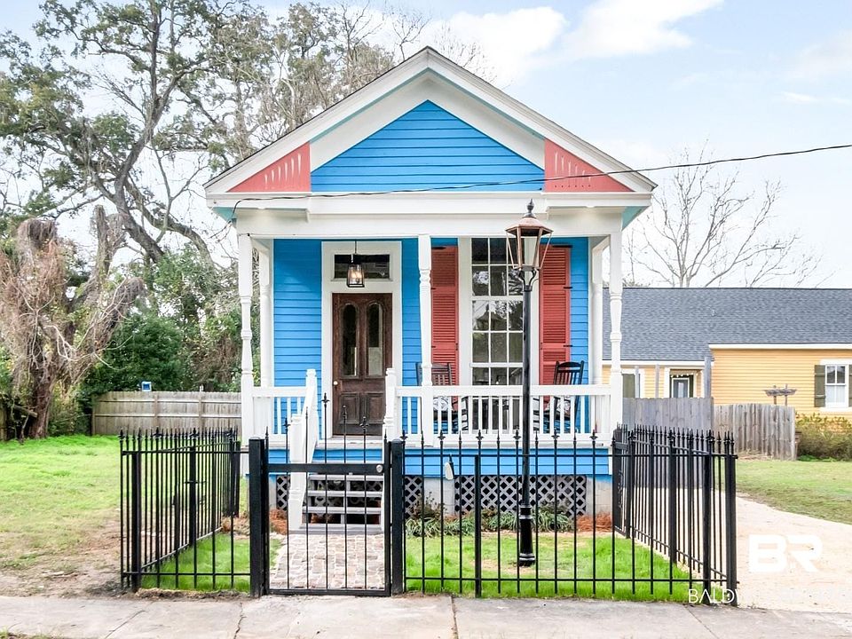 Shotgun-style home featuring a porch, a fenced front yard, and a gate