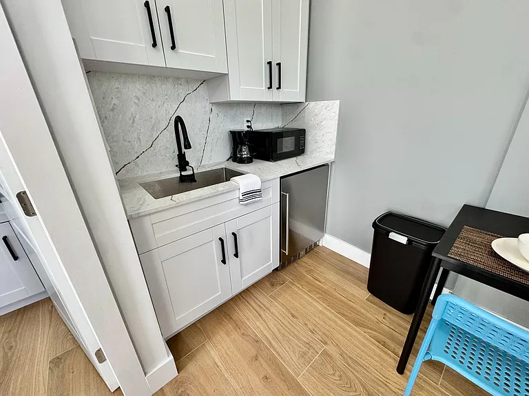Compact kitchenette with shaker cabinetry, stone-look counters, undermount sink, and included microwave and mini fridge.