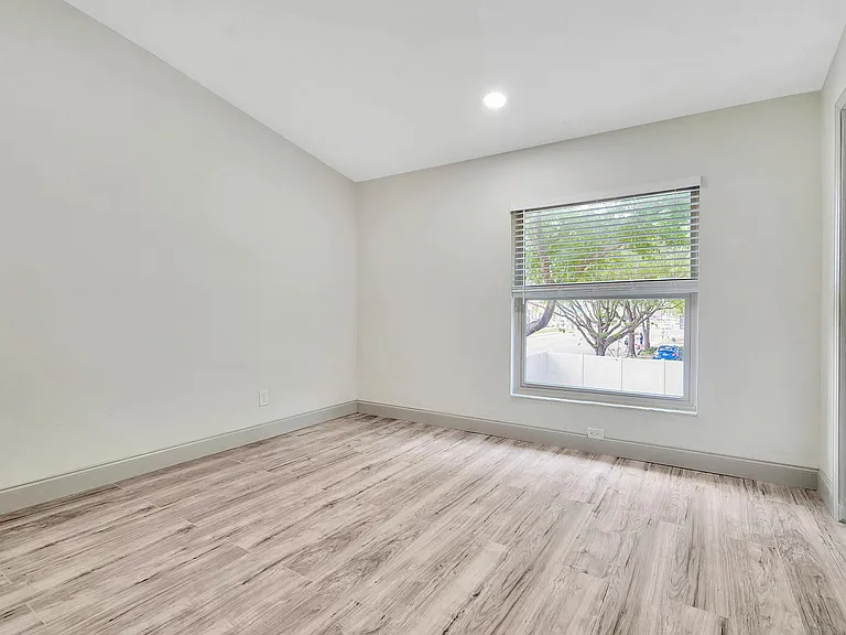 Bright and spacious room with sleek wood flooring and large window overlooking greenery.