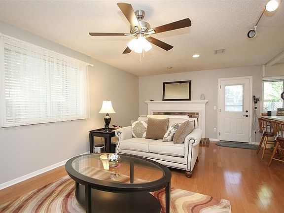 Enjoy a family night together with the family here in your lovely living room featuring a dark stained ceiling fan with lighting, wood floors, and large windows.