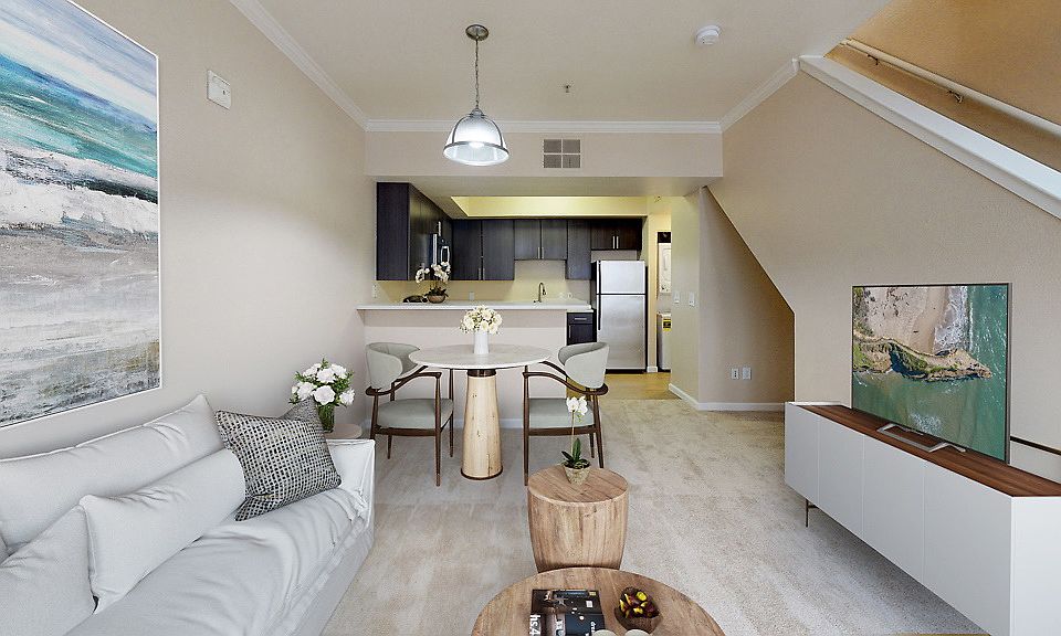 Staged living room and dining area with carpet, stairs to 2nd floor, and kitchen with stainless steel appliances.