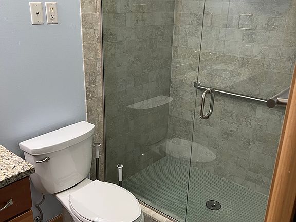 En-suite bathroom in primary bedroom. Rock tile floor and shower surround.