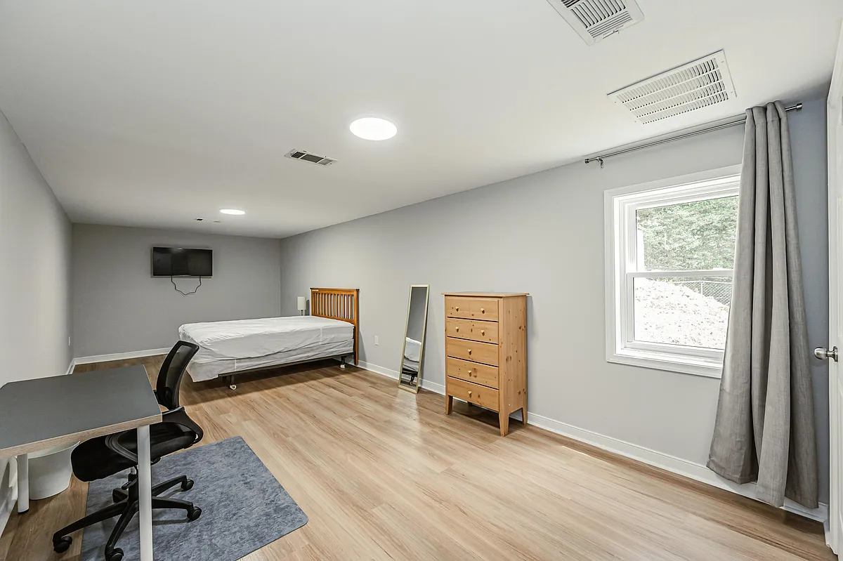 Photo 1 of 10 - Stratford Ct - Richmond, VA Spacious bedroom featuring hardwood floors, a large window with curtains, dresser storage, and a dedicated work desk. - Stratford Ct