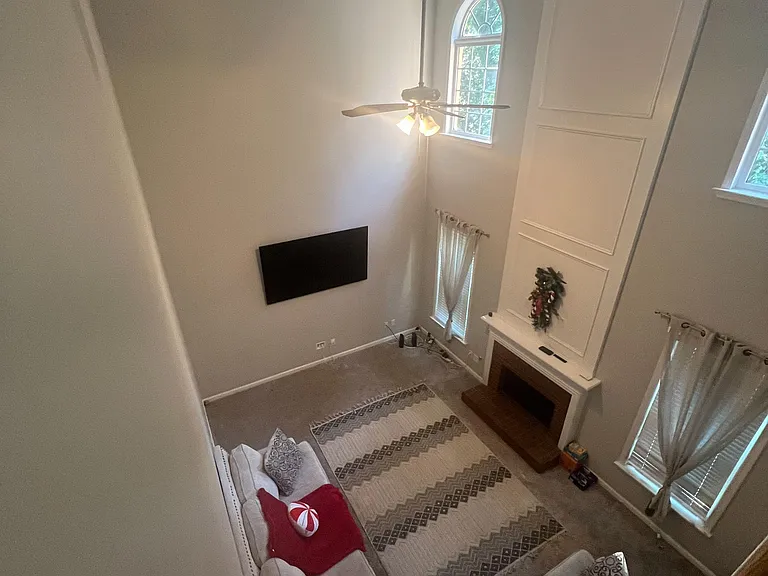 Double-height living room with ceiling fan, tall arched windows, and a fireplace centerpiece with wall-mounted TV.