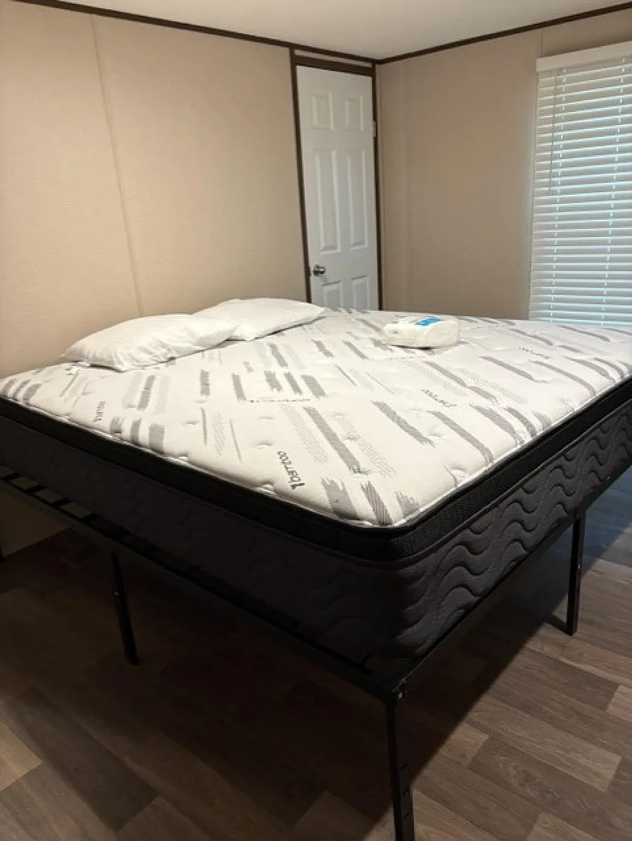 Private bedroom with a bed frame, neutral walls, and a window with blinds for light and privacy. - Eastern Ave