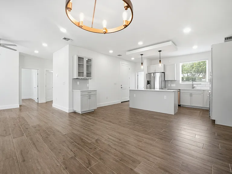 Bright open-concept living with abundant natural light. Modern kitchen features a large island, quartz countertops, and stainless steel appliances. A floating ceiling with integrated lighting above the island adds a warm, inviting ambiance.