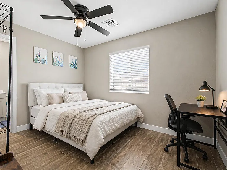 Furnished bedroom featuring a queen bed, wood-look flooring, ceiling fan, and a dedicated desk workspace near the window.
