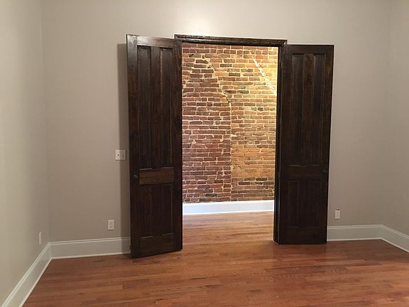 Large bedroom with double doors and brick wall with oak hardwood floors.