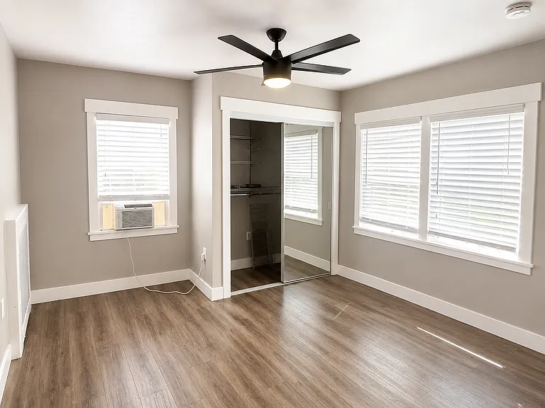 Spacious bedroom with large windows, ceiling fan, and abundant natural light.