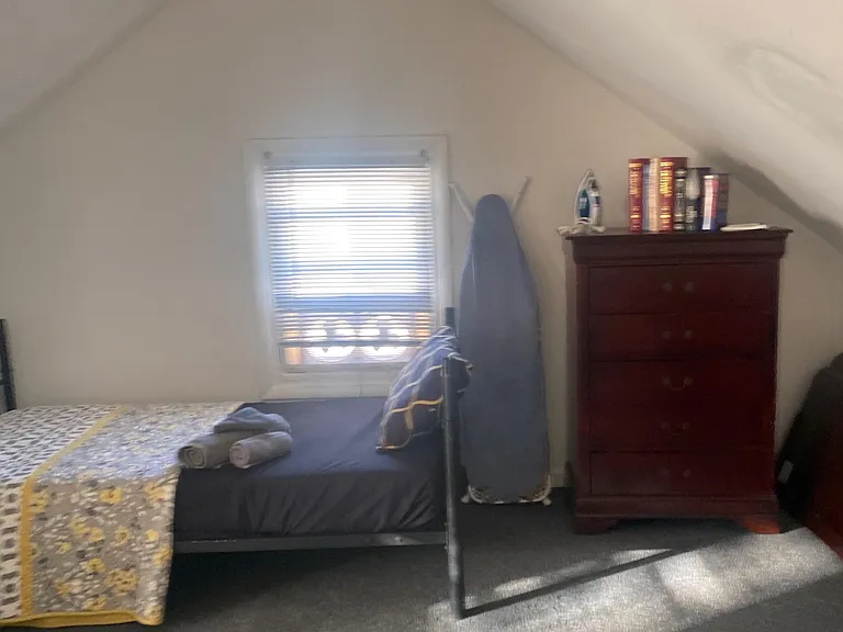 Attic-style bedroom with a low-slope ceiling, window with blinds, and space for a bed and dresser for everyday storage.