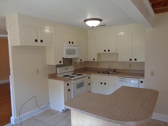 Island between kitchen and dining room, more cabinets behind photographer. Tile flooring.