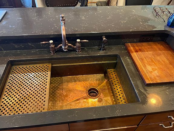 solid copper sink, with Waterstone faucet, drain grate on left, and soap caddy, cutting board on the right