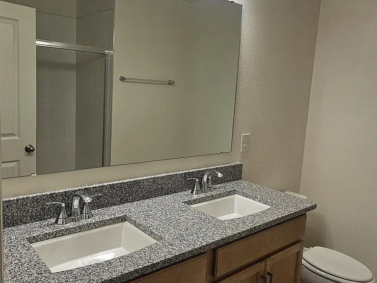 Primary bathroom featuring a dual-sink vanity with granite countertop, ample cabinet storage, and modern lighting.