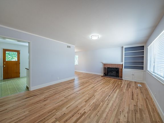 Main living room with wood burning fireplace, new paint, refinished hardwood floors, new baseboards, blinds, view into kitchen and dining room around the corner. The other pictures are older without refinished floors and baseboards.