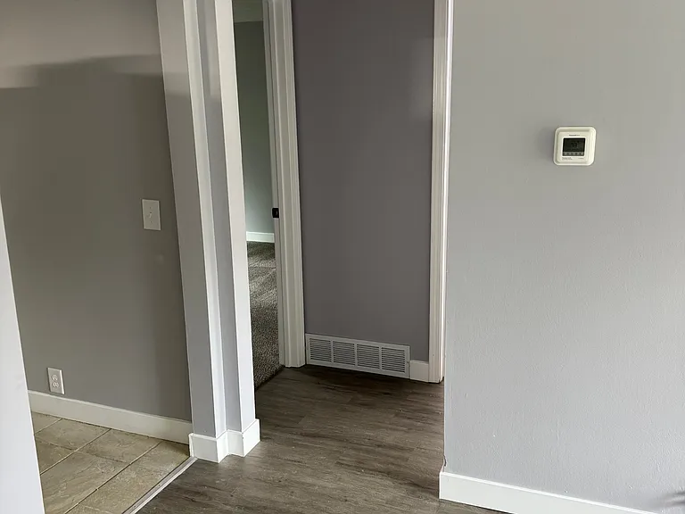 living room looking toward hall between bedrooms and bathroom with kitchen entry to the left. the picture distorts the paint on the walls it is all solid gray with white trim
