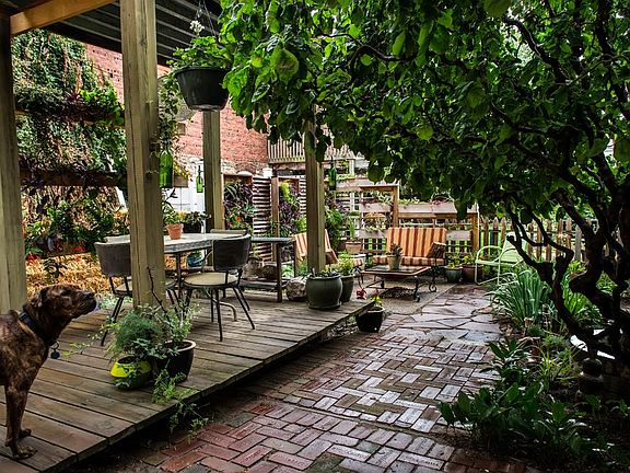 Elevated exterior Covered Pergola is surrounded by custom hanging planter boxes, planting beds and Coffeyville pavers. Lights continue around the perimeter of the base and top complimented by custom wine bottle tiki torches which flank the columns.