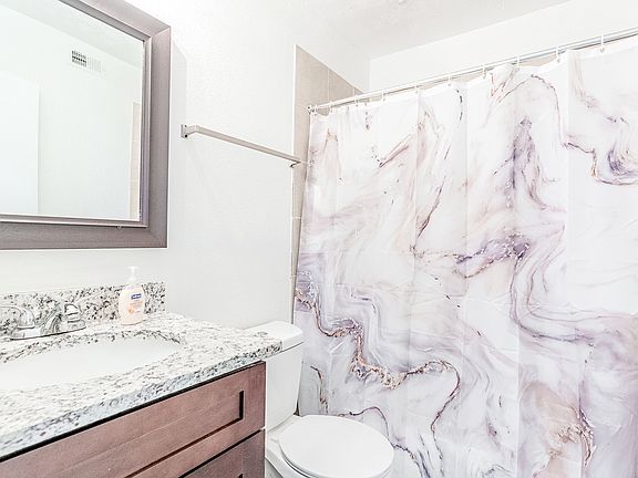 Spacious shared bathroom featuring commode, tub/shower combo and granite countertops.