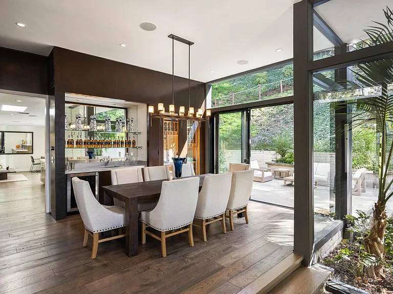 Dine in the stunning dining room surrounded by floor-to-ceiling glass walls, offering views of the lush greenery outdoors.