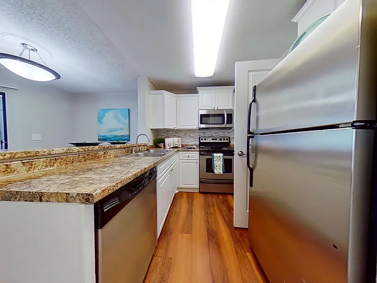 Enjoy a stylish kitchen in The Newport Autograph floor plan featuring stainless steel appliances, granite-style countertops, and a breakfast bar overlooking the living area.
