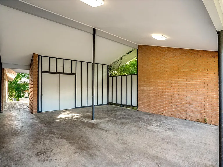 Covered parking area featuring a concrete surface, brick wall, and overhead lighting