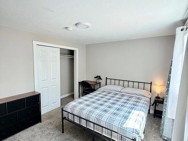 Furnished bedroom with a full bed, nightstand, dresser, and a work desk, plus a closet for convenient storage.