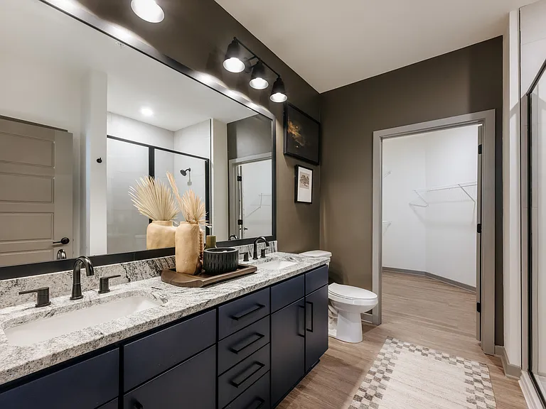 Luxury apartment bathroom with granite countertops, double vanity, semi-frameless glass shower, and spacious walk-in closet.