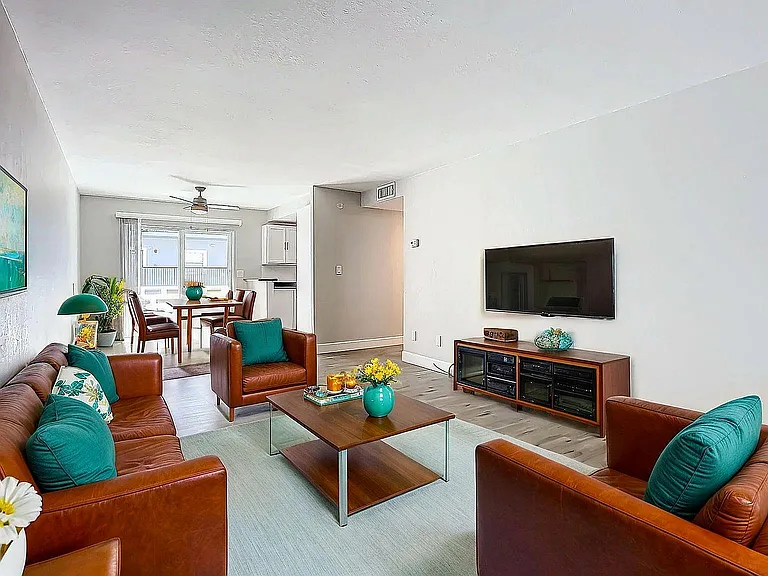 Contemporary living room with sleek leather furniture, vibrant teal accents, and open dining area, flooded with natural light.
