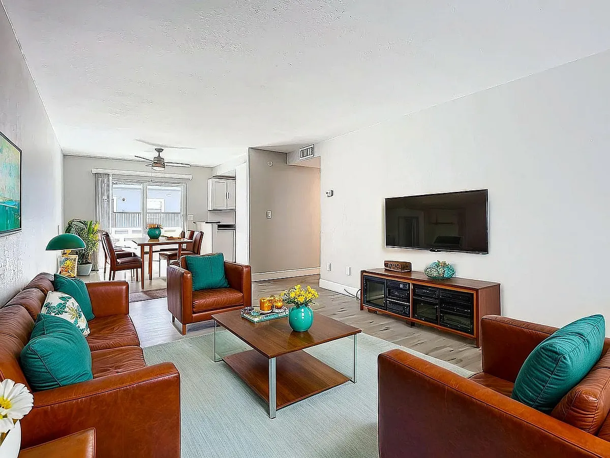 Contemporary living room with sleek leather furniture, vibrant teal accents, and open dining area, flooded with natural light. - The Sea Glass