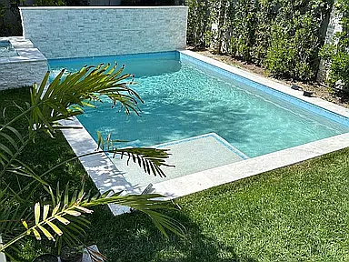 Pool surrounded by marble pavers with linear fountain off marble ledger stone wall