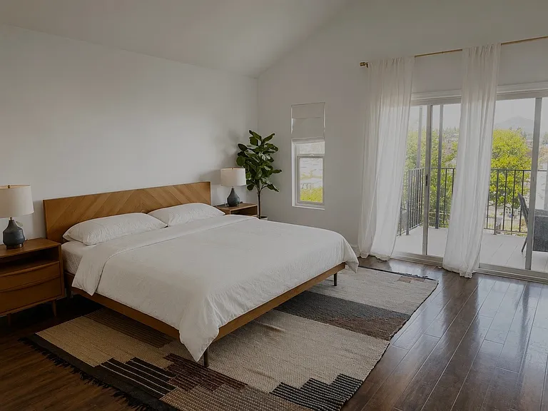 Spacious primary suite featuring vaulted ceilings, rich wood flooring, a private view balcony, and abundant natural light. The serene retreat offers the perfect place to unwind while enjoying peaceful easterly views and refreshing morning sunrises.