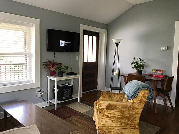 Living room. West Elm couch, wall mount smart TV, West Elm table. Door opens to long porch overlooking driveway.