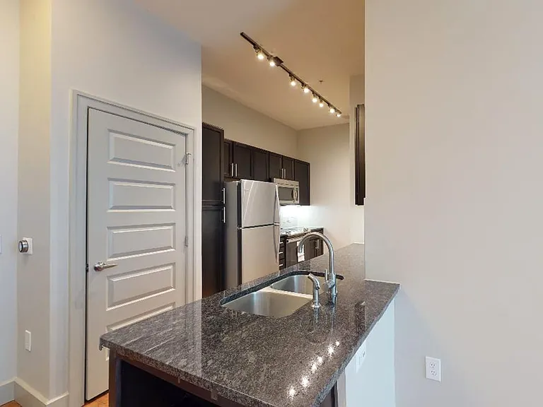 Apartment kitchen with stainless steel appliances, granite countertops and wood-style flooring.