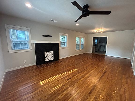 Spacious room featuring wood flooring, a fireplace with a decorative screen and black brick surround, recessed lighting, and a ceiling fan
