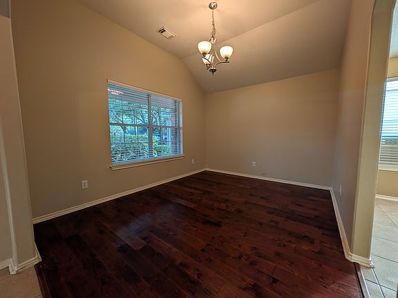Spacious formal dining area featuring beautiful dark wood floors, elegant lighting, and a soaring vaulted ceiling that creates an open, airy ambiance.
