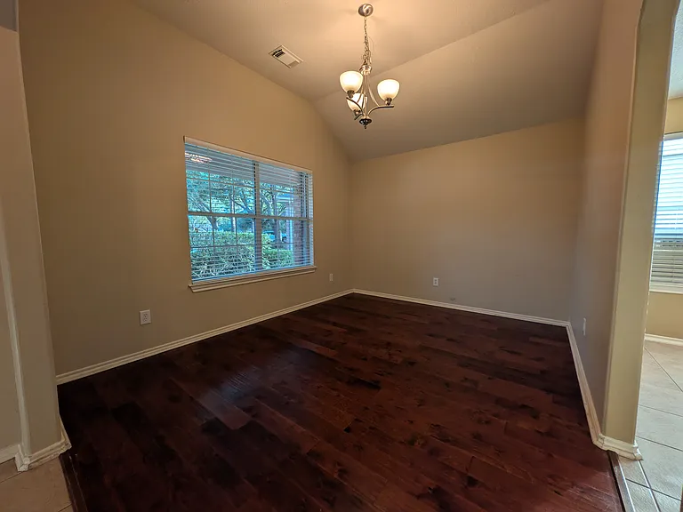 Spacious formal dining area featuring beautiful dark wood floors, elegant lighting, and a soaring vaulted ceiling that creates an open, airy ambiance.